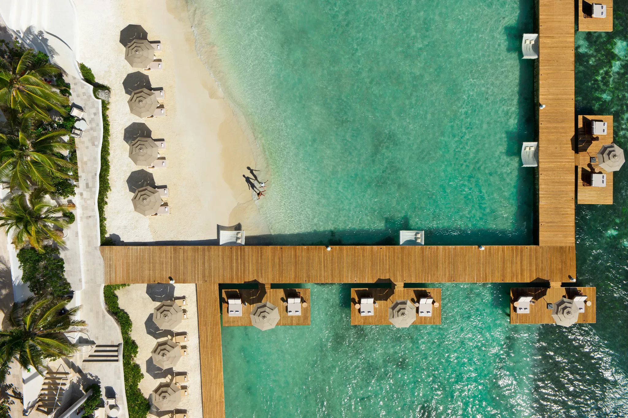 Top-down aerial of beach and private overwater decks at Impression Isla Mujeres by Secrets with white sand and clear water.
