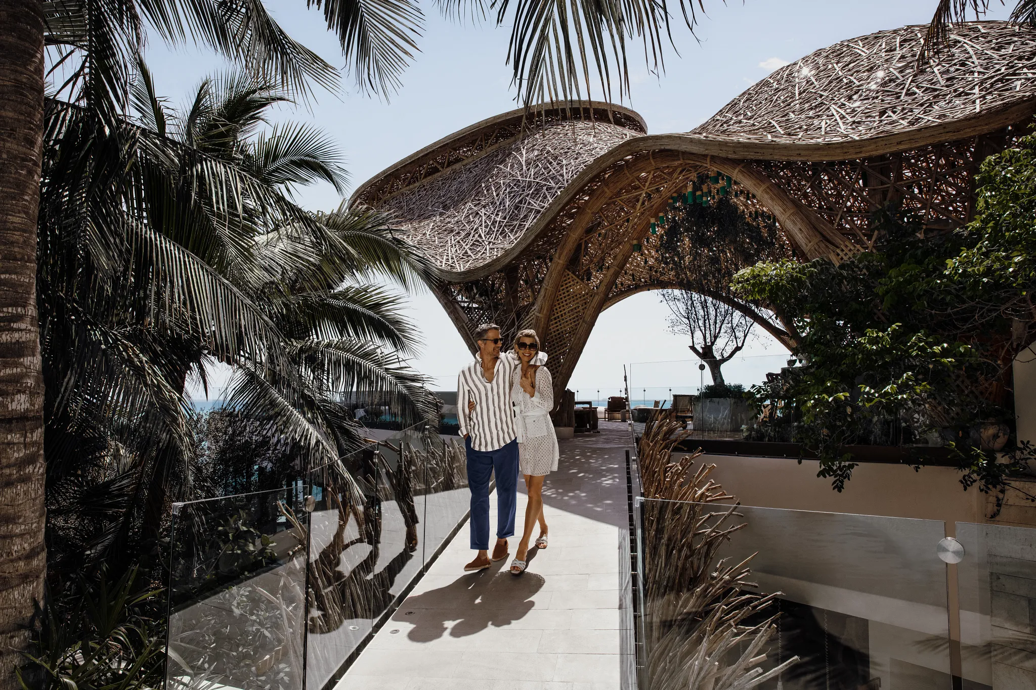 Couple walking across a modern bridge under a sculptural canopy at Impression Isla Mujeres by Secrets.