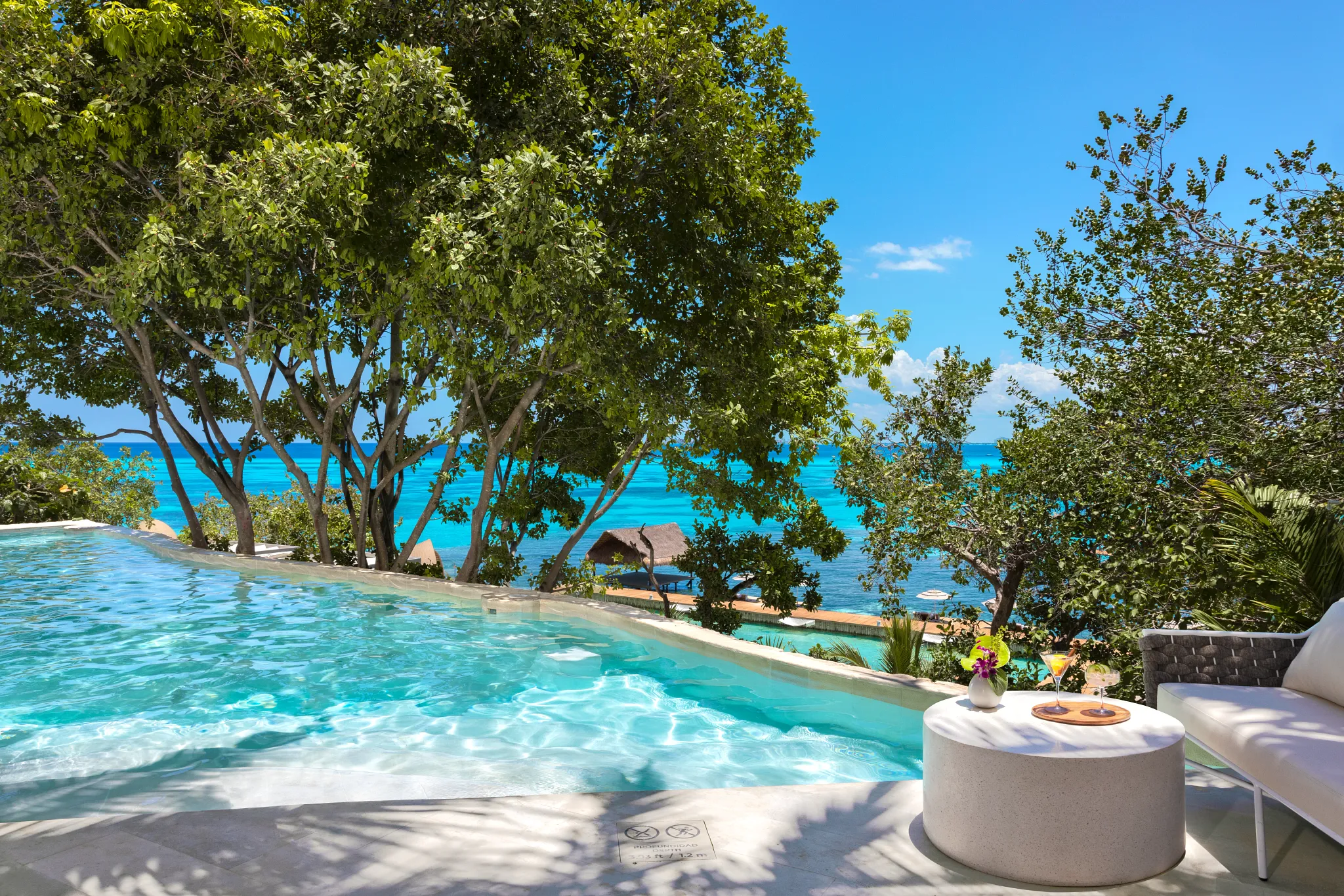 Elevated infinity pool surrounded by tropical trees with ocean view at Impression Isla Mujeres by Secrets.