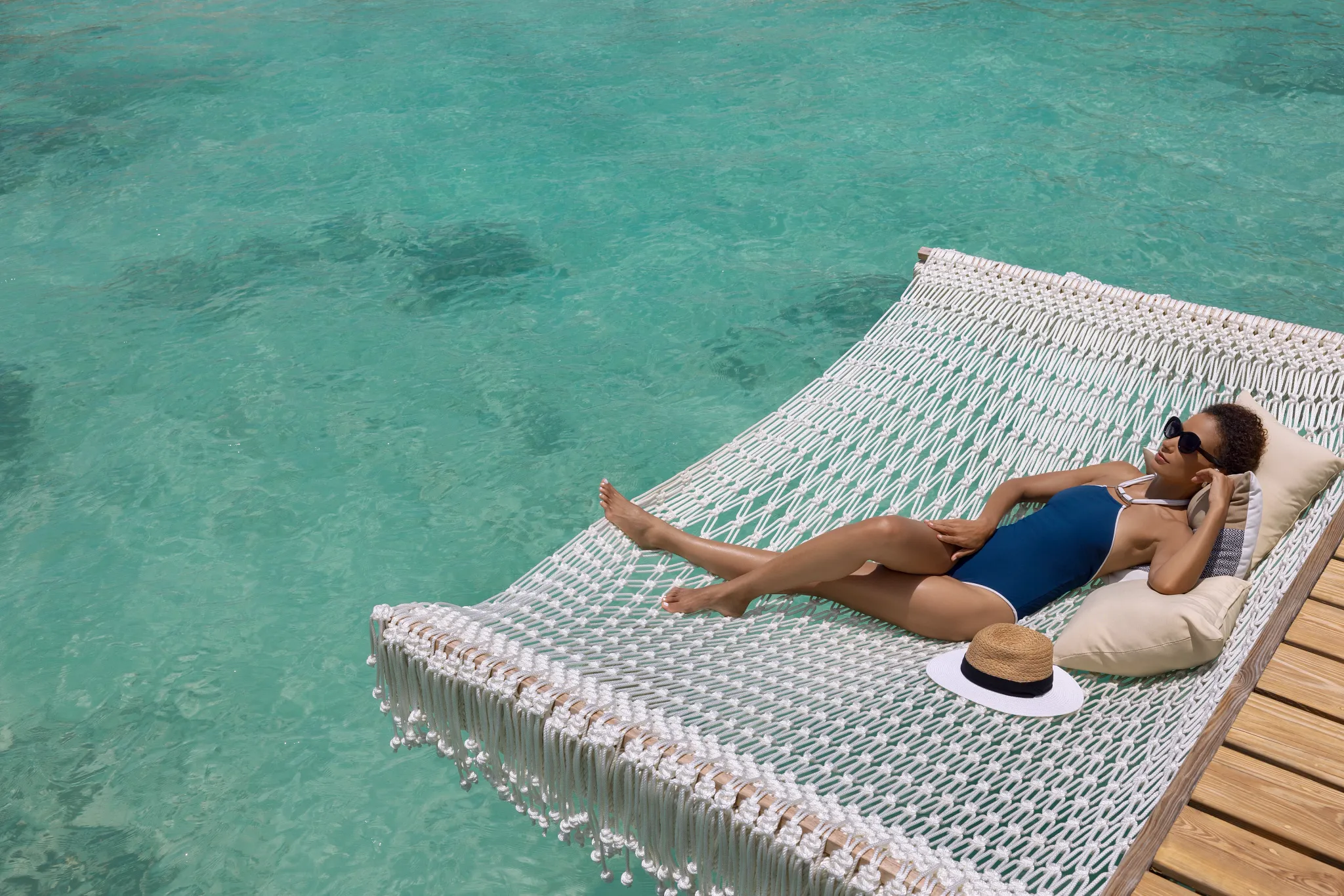 Woman relaxing on a hammock over turquoise water at Impression Isla Mujeres by Secrets.