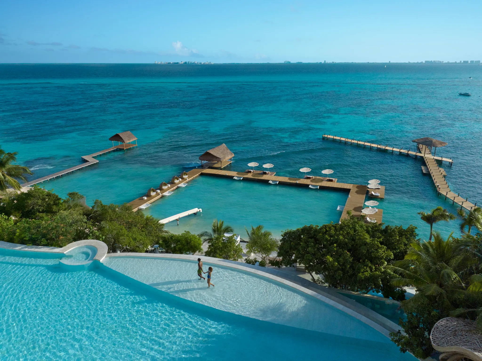 Aerial view of infinity pool and overwater decks at Impression Isla Mujeres by Secrets with vibrant blue sea.