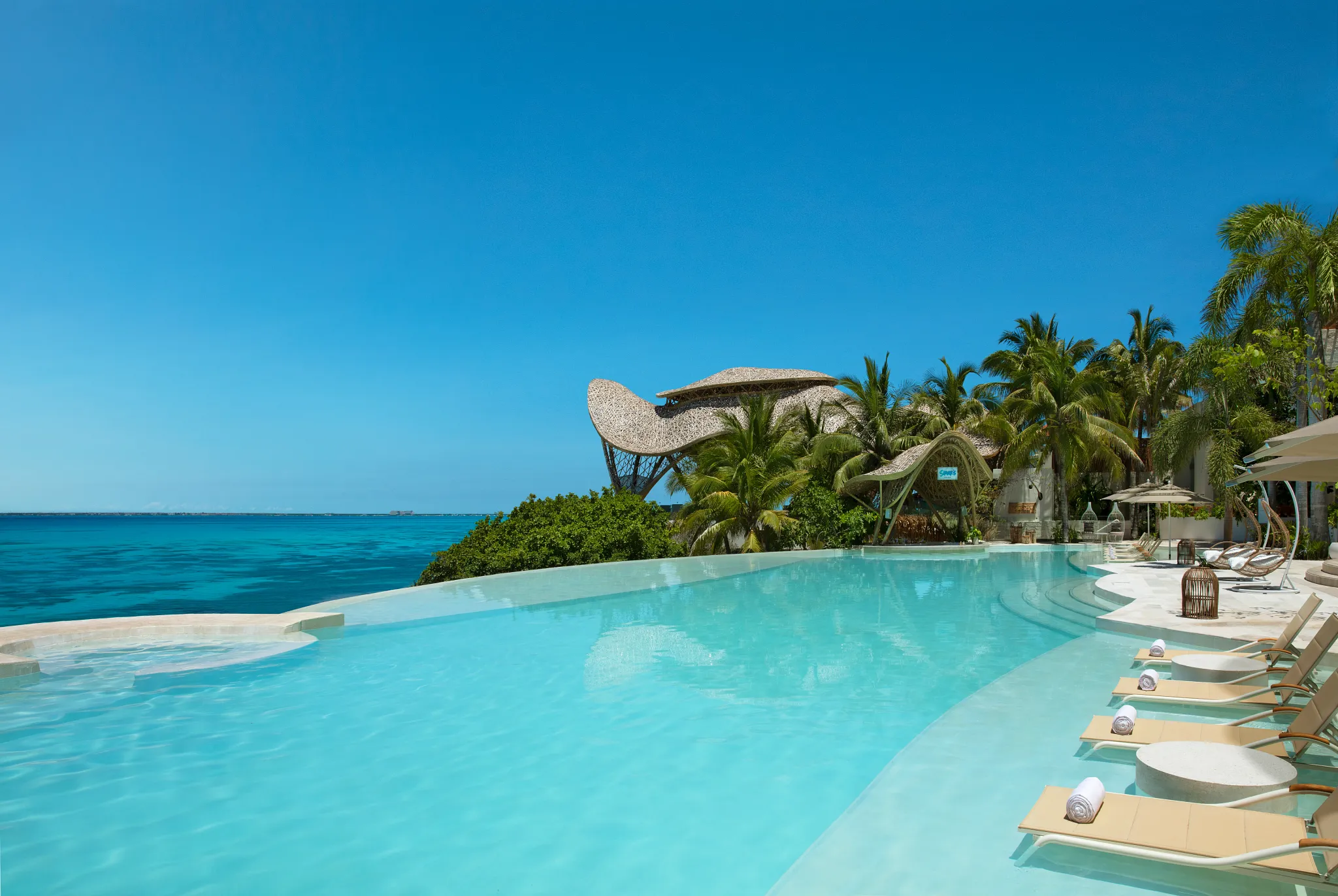 Curved infinity pool overlooking the ocean at Impression Isla Mujeres by Secrets with tropical surroundings.