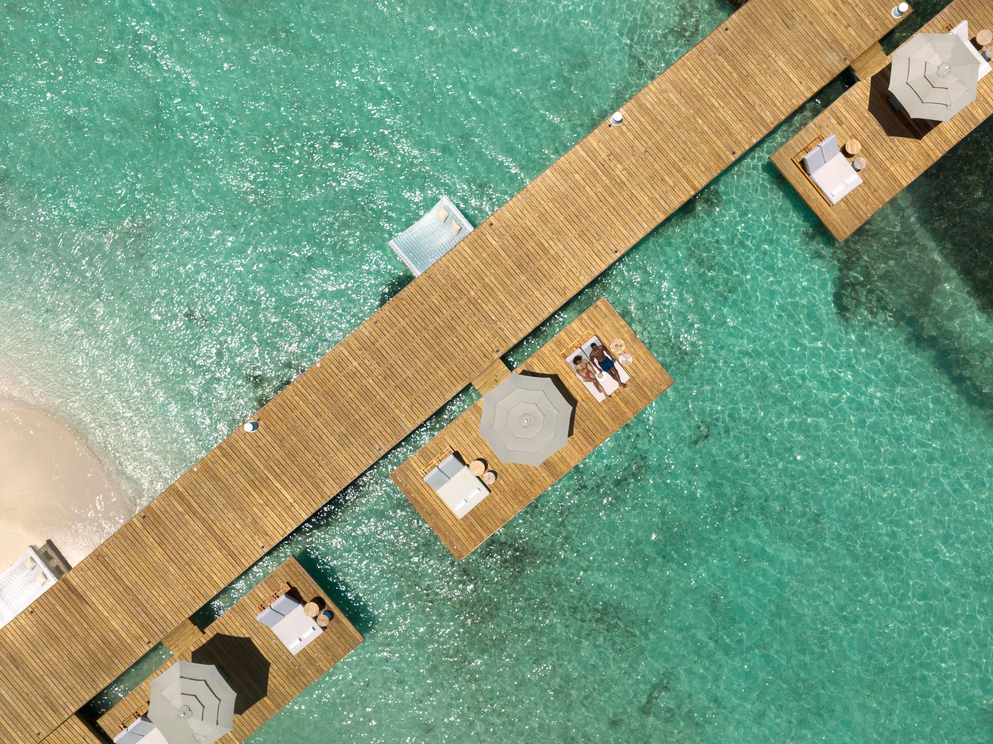 Aerial view of wooden overwater platforms and cabanas at Impression Isla Mujeres by Secrets above turquoise sea.