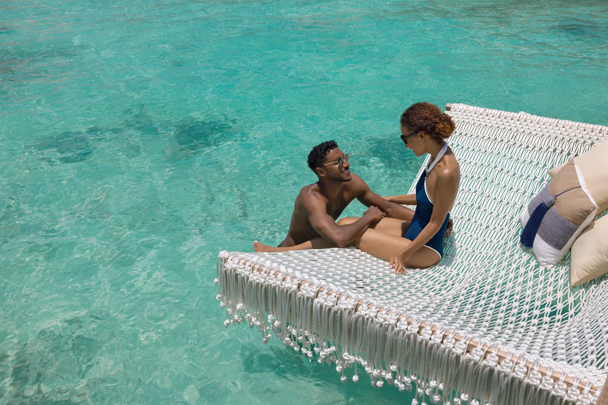 Couple relaxing on an overwater hammock above crystal-clear turquoise water at Impression Isla Mujeres by Secrets.