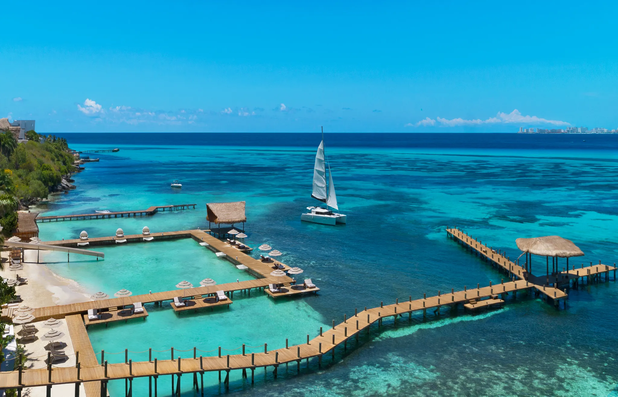 Aerial view of piers and overwater platforms with a sailboat near Impression Isla Mujeres by Secrets.