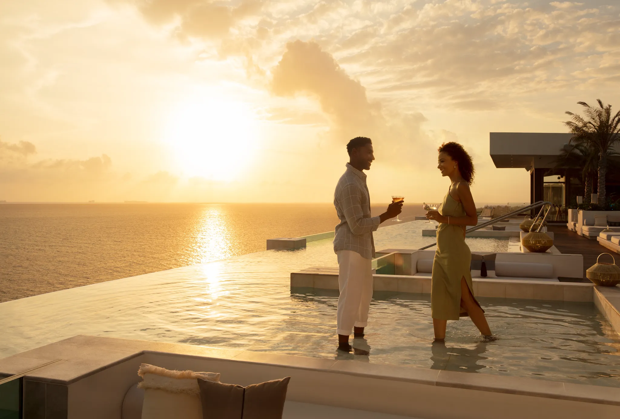 Couple enjoying sunset cocktails in a rooftop infinity pool at Impression Isla Mujeres by Secrets, overlooking the Caribbean Sea.