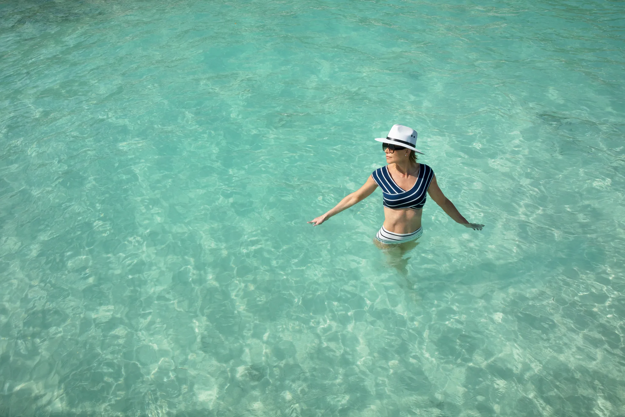 Woman standing in shallow crystal-clear ocean water wearing sunhat at Impression Isla Mujeres by Secrets.